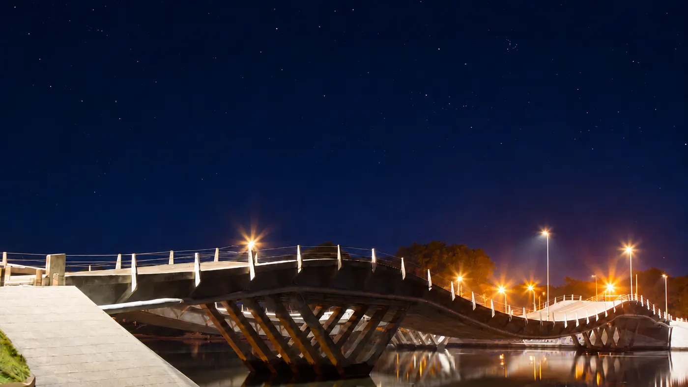 El puente ondulado de La Barra sobre el arroyo Maldonado, de noche, iluminado por sus faroles bajo un cielo estrellado