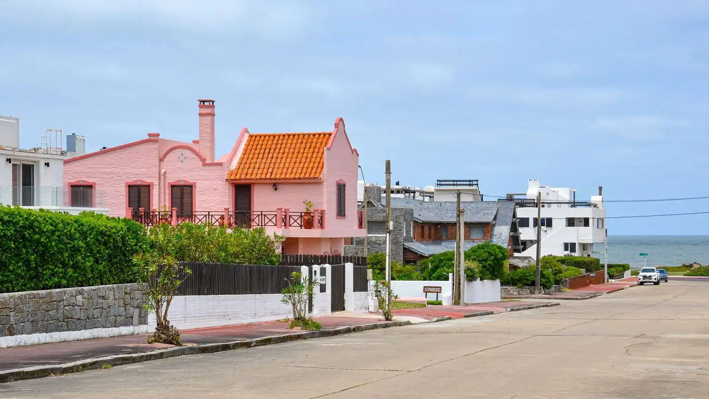 Calle de Punta del Este con una casa rosada de techo de tejas y el mar al fondo