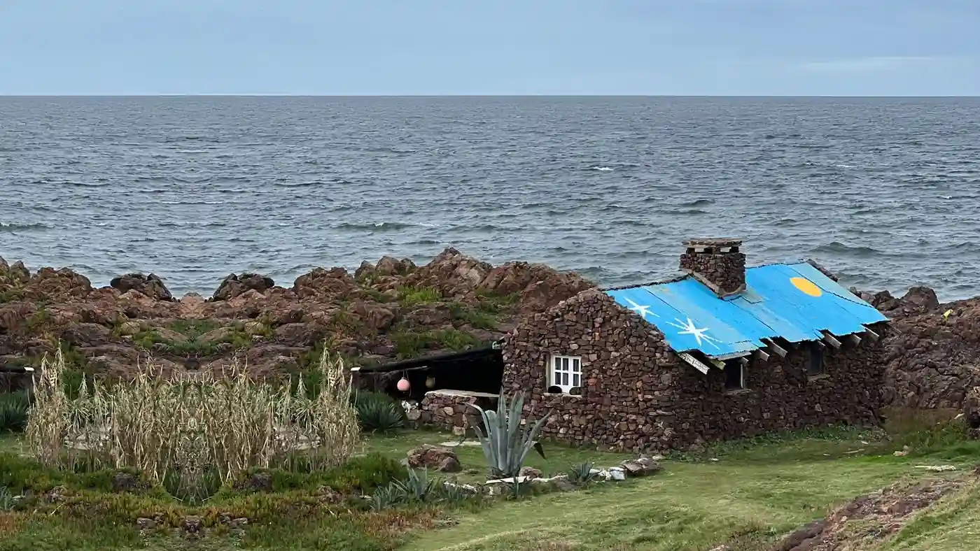 Una casa de piedra con el techo pintado de azul, frente al mar abierto, en la costa de Maldonado