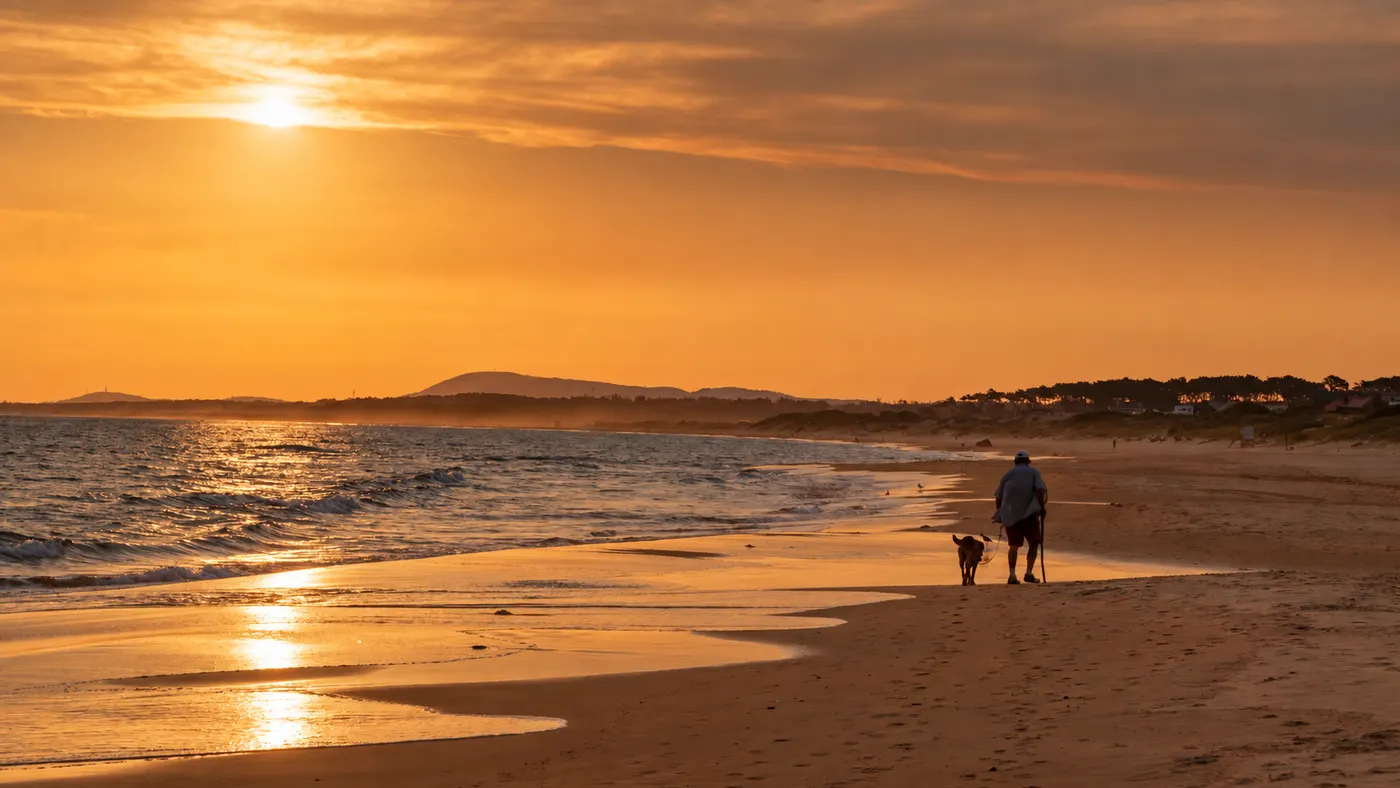 An empty beach near José Ignacio, Uruguay, at sunset, with the ocean on the left and a lone walker with a dog far down the shore