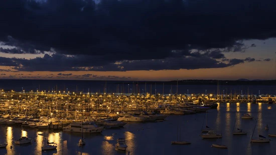 The Punta del Este marina at dusk, dozens of sailboats and yachts lit in warm light under a storm sky