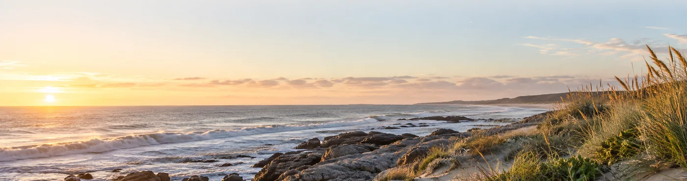 Costa atl&aacute;ntica de Maldonado al atardecer, con mar, rocas y vegetaci&oacute;n de dunas